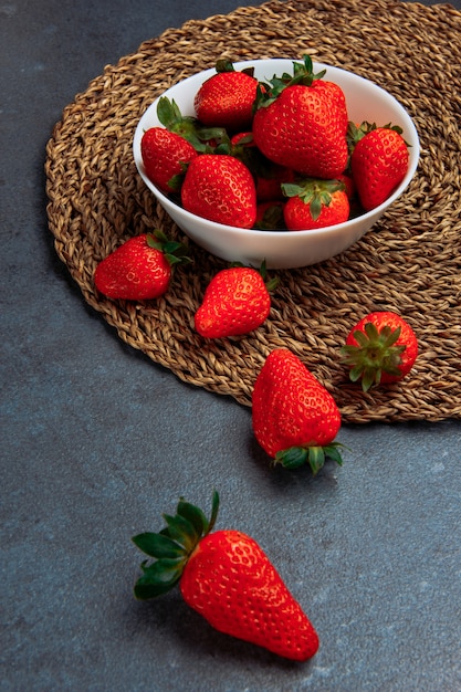 Fresas de buen gusto en un tazón blanco vista de ángulo alto sobre un fondo de mantel gris y redondo