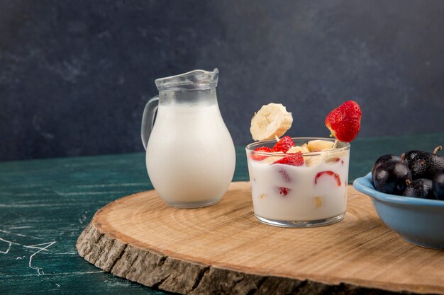 Fresas en crema servidas con leche y cerezas en una bandeja de madera