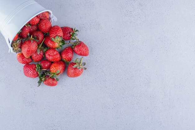 Fresas derramándose de un pequeño balde sobre fondo de mármol. Foto de alta calidad