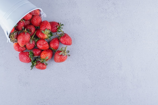 Fresas derramándose de un pequeño balde sobre fondo de mármol. Foto de alta calidad