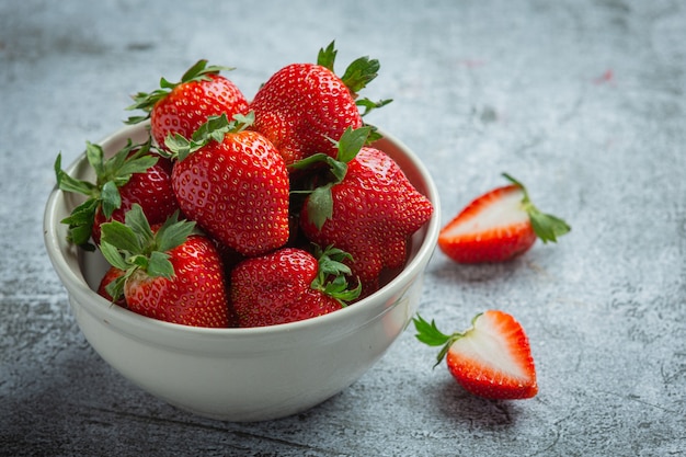 Fresas frescas en un recipiente sobre fondo oscuro antiguo