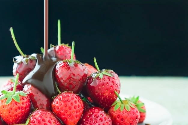 Fresas frescas con verter el chocolate derretido sobre fondo negro