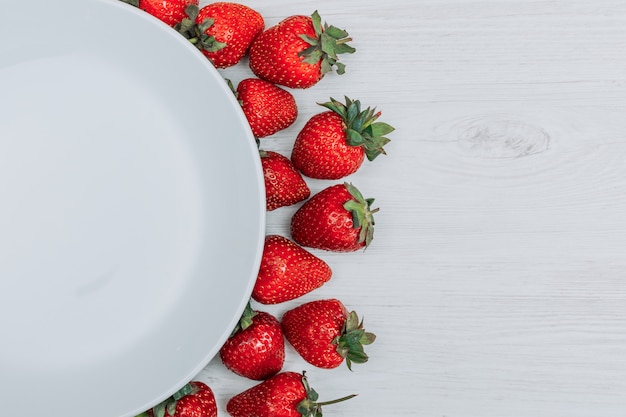 Fresas del primer con la placa vacía en el fondo de madera blanco. espacio de copia horizontal para texto