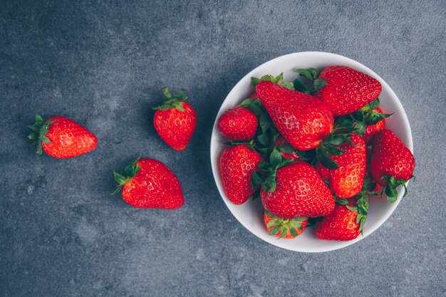 Fresas en un recipiente sobre un fondo gris con textura. vista superior.