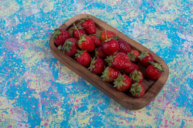 Fresas rojas en una bandeja de madera sobre fondo azul.