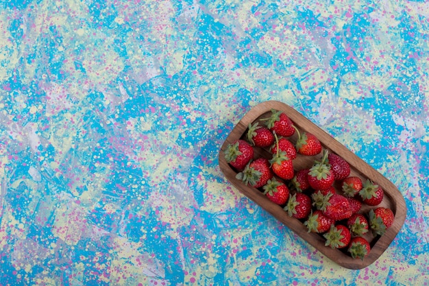 Fresas rojas en una bandeja de madera sobre la mesa azul, vista superior