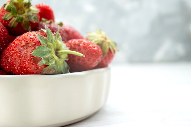 Fresas rojas frescas bayas suaves y deliciosas dentro de la placa blanca en el escritorio de luz, color rojo baya de fruta