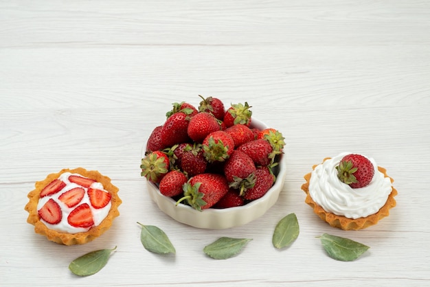 Foto gratuita fresas rojas frescas bayas suaves y deliciosas dentro de la placa con tortas en la mesa de luz