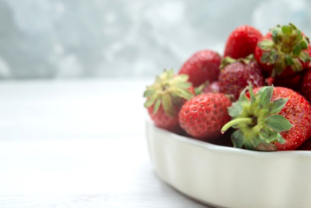 Fresas rojas frescas bayas suaves y deliciosas dentro de un plato blanco a la luz, color rojo de la foto de la baya de la fruta