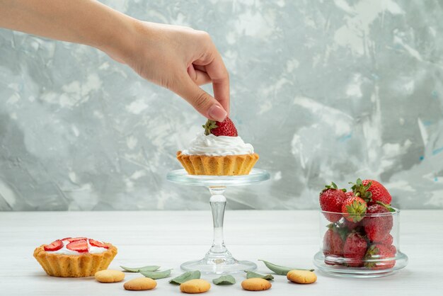 Fresas rojas frescas bayas suaves y deliciosas con pasteles y galletas en el escritorio gris claro