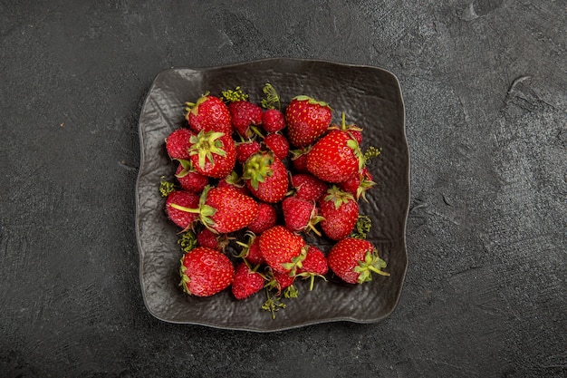 Fresas rojas frescas de la vista superior dentro de la placa en la baya de la fruta de la mesa oscura