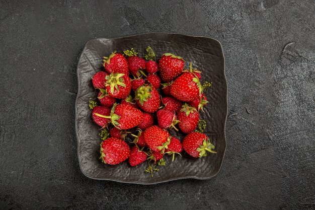 Fresas rojas frescas de la vista superior dentro de la placa en la baya de la fruta de la mesa oscura