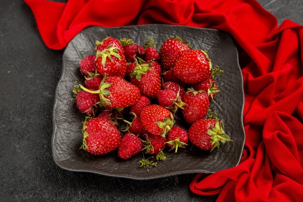 Fresas rojas frescas de la vista superior dentro de la placa en la baya de la fruta de la mesa oscura