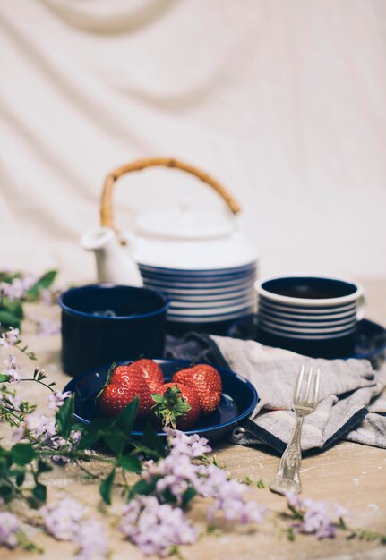 Fresas rojas; Juego de té y desenfoque de flores en el escritorio de madera