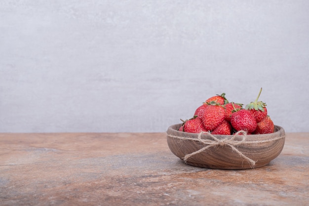 Fresas rojas en una taza de madera rústica.