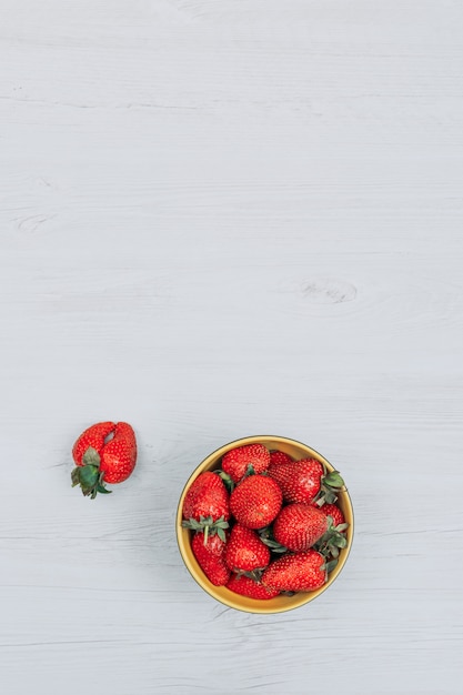 Foto gratuita fresas en un tazón amarillo con una fresa plana yacía sobre un fondo de madera blanca copia espacio para texto