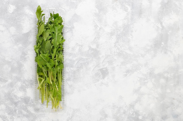 Foto gratuita frescas hojas de rúcula o rúcula verde en cajas de plástico sobre hormigón gris