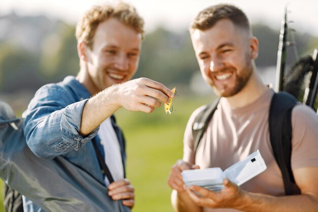 Friends está listo para pescar. Hombres sosteniendo un equipo de pesca y mirando en una caja blanca con cebo para peces. Un hombre vestido con camiseta rosa y otro camiseta azul