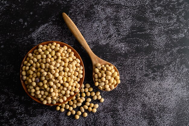 Frijoles amarillos en un tazón de madera y cuchara de madera en el piso de cemento negro.