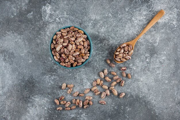 Frijoles crudos y cuchara de madera sobre mármol.