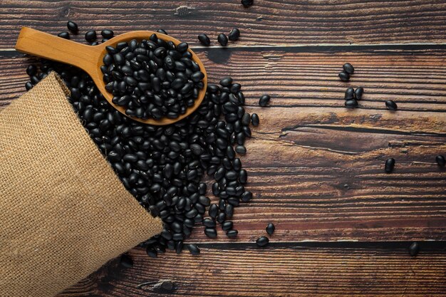 Frijoles negros en una pequeña cuchara de madera, coloque junto a la bolsa de saco llena de frijoles negros