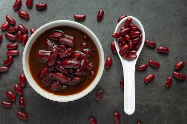 Foto gratuita frijoles rojos hervidos en un tazón blanco con semillas de frijoles rojos en una cuchara en el piso oscuro