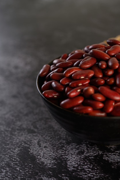 Frijoles rojos en un recipiente de madera en el piso de cemento negro.