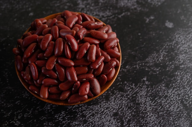 Frijoles rojos en un recipiente de madera en el piso de cemento negro.