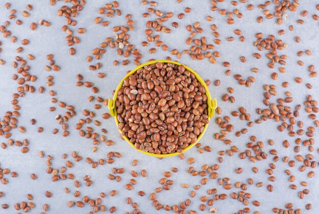 Frijoles rojos secos rellenos y esparcidos alrededor de un pequeño balde sobre una superficie de mármol