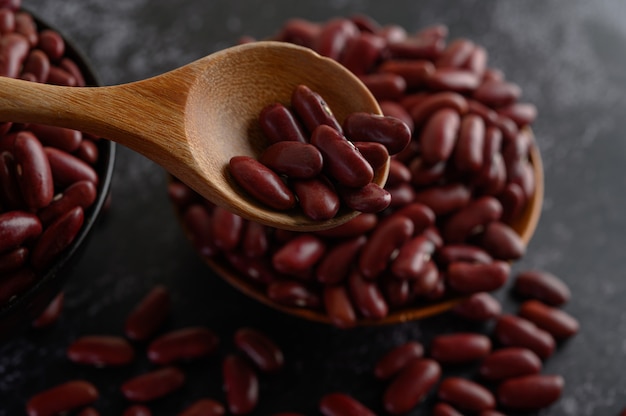 Frijoles rojos en un tazón de madera y cuchara de madera en el piso de cemento negro.