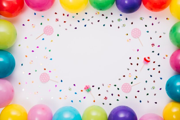 Frontera de globos de colores con confeti y accesorios sobre fondo blanco