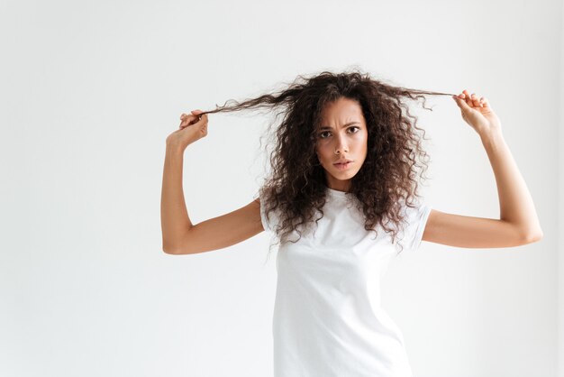 Frunciendo el ceño mujer insatisfecha tocando su cabello y mirando a cámara