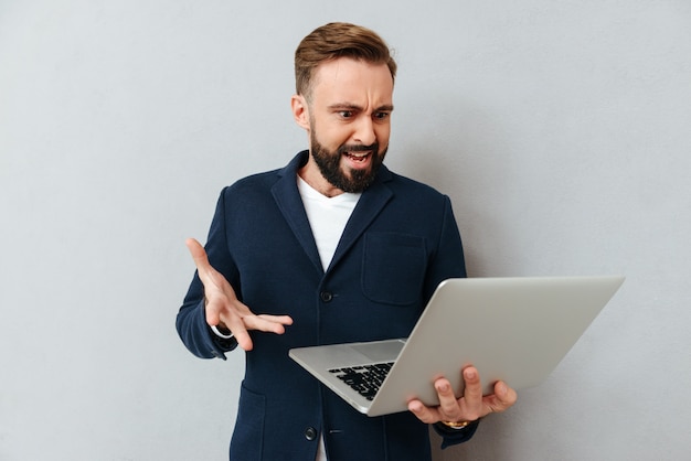 Fruncir el ceño hombre serio en traje usando laptop aislado