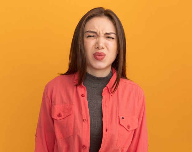 Fruncir el ceño joven bonita frunciendo los labios aislados en la pared naranja