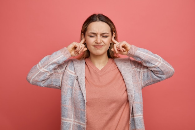 Fruncir el ceño joven poniendo los dedos en los oídos con los ojos cerrados