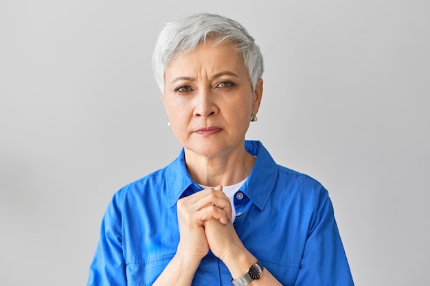 Foto gratuita frustrada preocupada mujer madura de pelo gris cogidos de la mano en el pecho, con expresión facial incómoda, preocupándose por su marido que está enfermo. emociones, reacciones y lenguaje corporal humanos