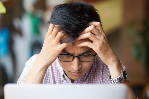 Frustrado joven asiático sentado en la computadora portátil