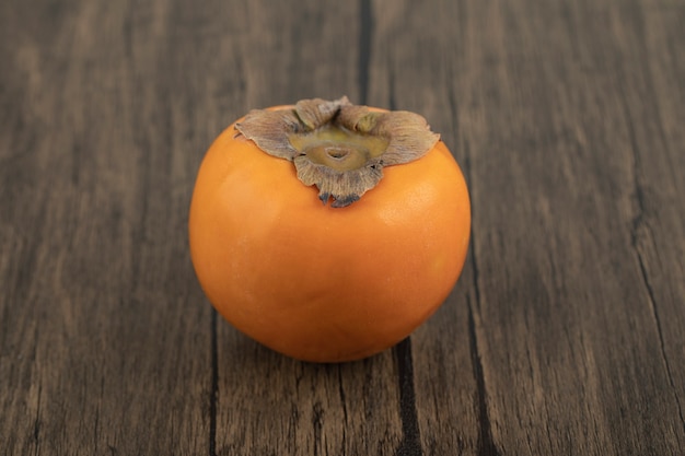 Una fruta de caqui madura colocada sobre una superficie de madera