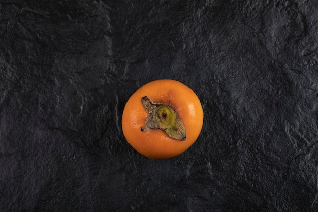 Una fruta de caqui madura colocada sobre una superficie negra