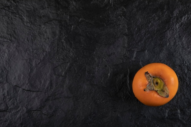 Foto gratuita una fruta de caqui madura colocada sobre una superficie negra