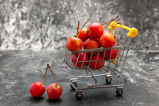 Fruta de cereza roja fresca en carrito de compras sobre fondo gris