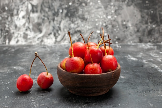 Fruta de cereza roja fresca en un recipiente marrón sobre fondo gris