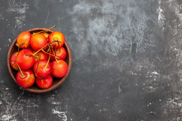 Fruta de cereza roja fresca en un recipiente marrón sobre fondo gris