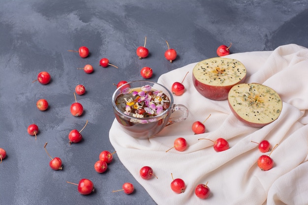 Fruta cortada a la mitad, cerezas y vaso de jugo con una rodaja de limón y flores en azul con mantel