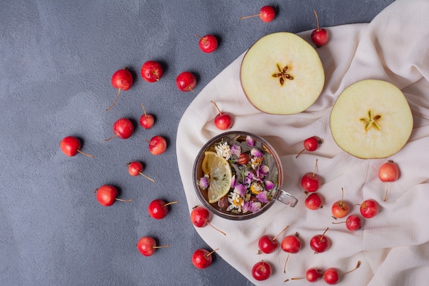 Fruta cortada a la mitad, cerezas y vaso de jugo con una rodaja de limón y flores en azul con mantel