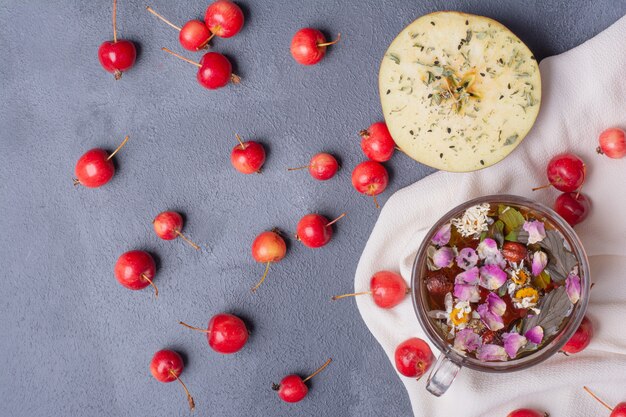 Fruta cortada a la mitad, cerezas y vaso de jugo con una rodaja de limón y flores en azul con mantel