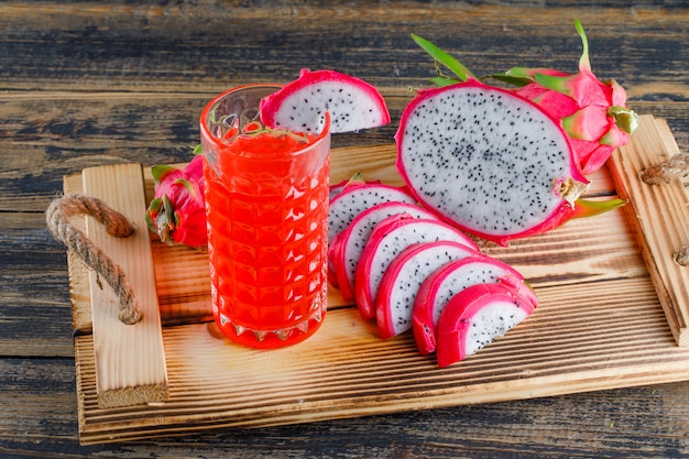 Fruta del dragón en una bandeja con vista de ángulo alto de jugo en una mesa de madera