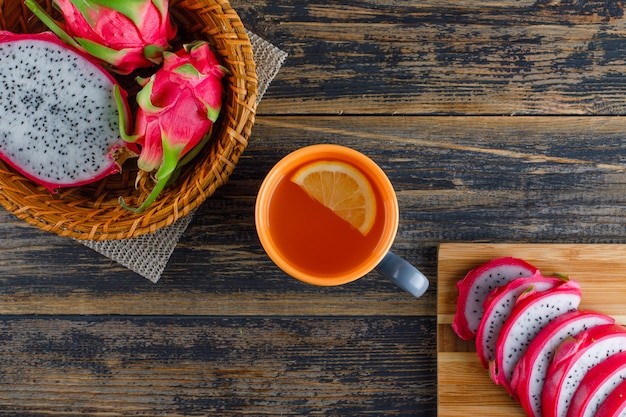 Fruta del dragón en una cesta con tabla de cortar, té plano sobre mesa de madera