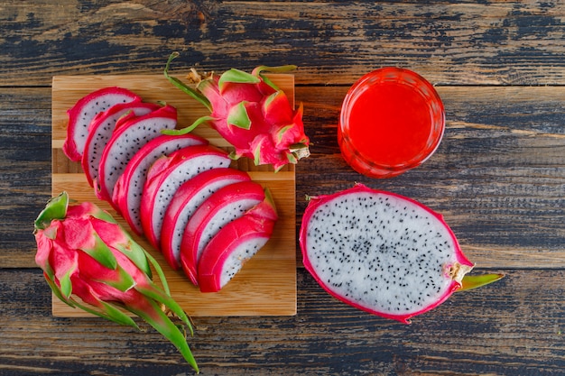 Foto gratuita fruta del dragón con jugo plano sobre madera y tabla de cortar