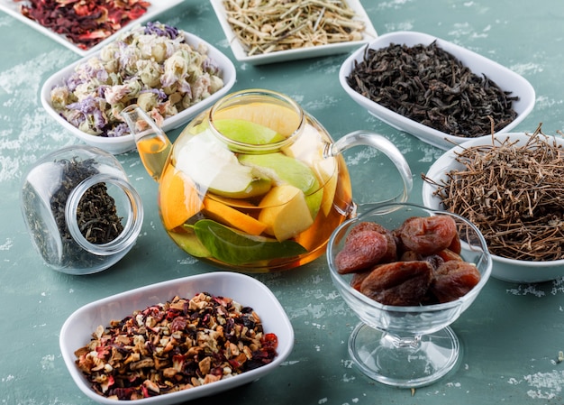 Fruta infundida de agua con albaricoques secos, hierbas, tallos de cereza en una tetera sobre la superficie de yeso